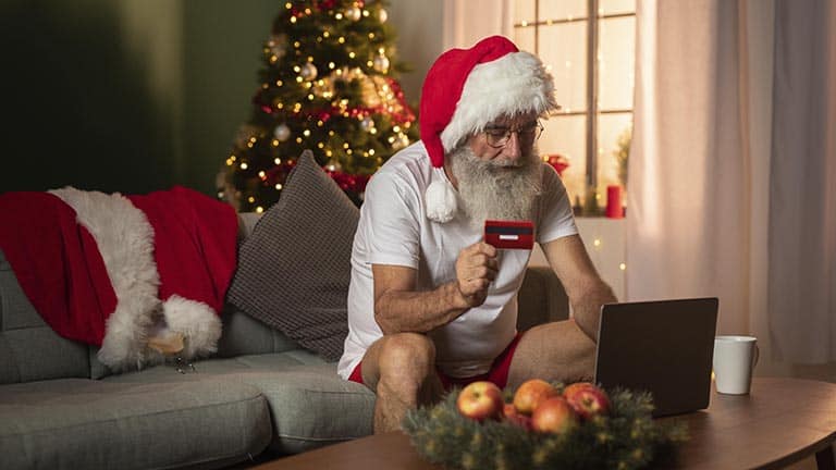 Tomte sitter och beställer julklappar på internet med kreditkort i ena handen